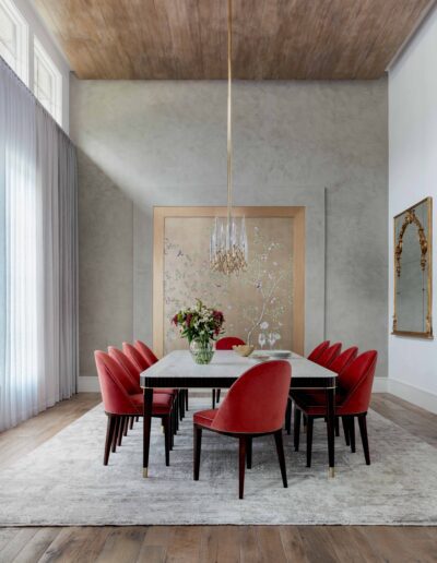 Elegant dining room with a white marble table, red chairs, and a large abstract painting on the wall under a crystal chandelier.
