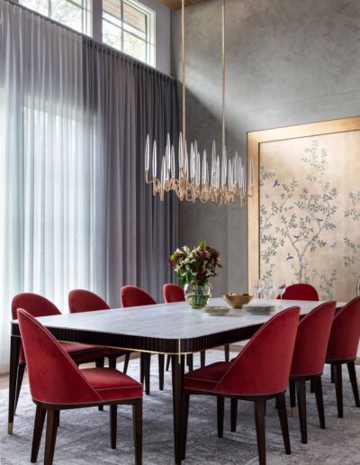Elegant dining room featuring a white marble table, red chairs, gold accents, and a unique chandelier, with a floral art panel on the wall.