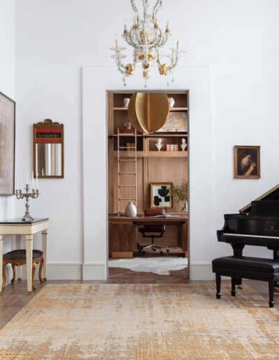 Elegant living room with a grand piano, antique furniture, an ornate chandelier, and a bookshelf built into a wall alcove.