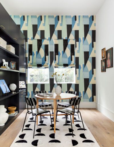 A modern dining room featuring a geometric patterned wall in blue and green, a round table with chairs, and stylish shelving filled with decor.