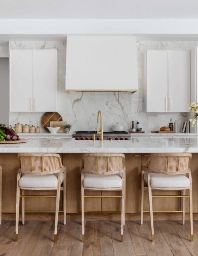 A modern kitchen with white cabinetry, marble backsplash, and a central island with woven bar stools.