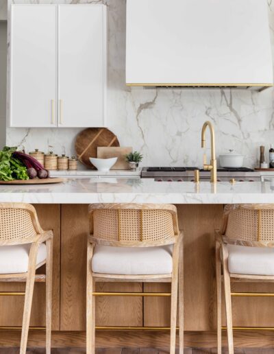 Modern kitchen interior with marble backsplash, wooden cabinetry, and rattan bar stools at a kitchen island.