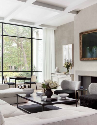 Modern living room with large windows, white sofas, a black coffee table, and minimalist decor, overlooking a green garden.