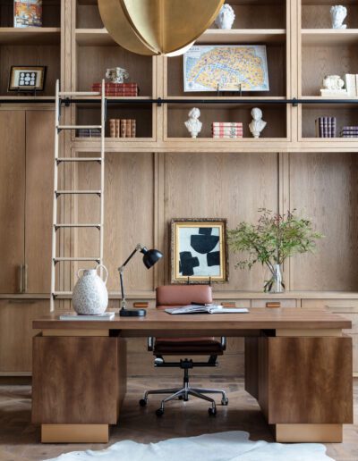 A well-organized home office with a large wooden desk, bookshelves, and a rolling ladder. decor includes a globe, artwork, and plants.