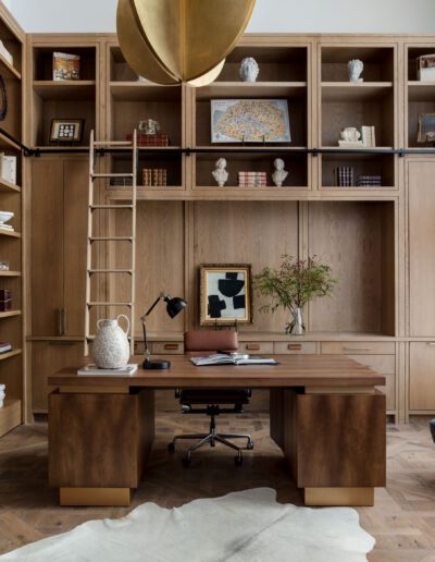 A spacious home office with a large wooden desk, surrounded by floor-to-ceiling shelves, a ladder, and chic furniture.