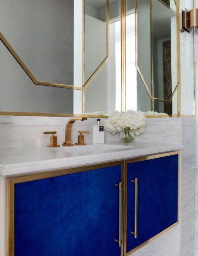 Modern bathroom vanity with blue cabinets, gold handles, and a marble countertop, flanked by geometric mirrors and a brass faucet.